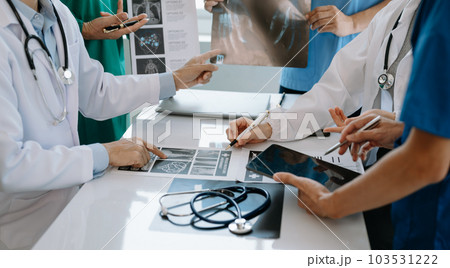 Medical team having a meeting with doctors in white lab coats and surgical scrubs seated at a table discussing a patients working online using computers in the medical industry 103531222