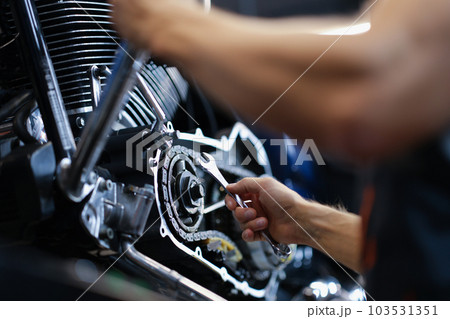 Male mechanic repairs amotorcycle motor with wrench in service center Male mechanic repairs amotorcycle motor with wrench in service center 103531351