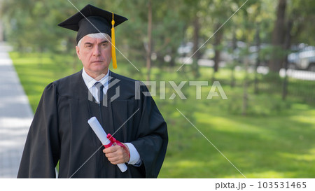 Serious old man in graduation gown holding diploma outdoors. Serious old man in graduation gown holding diploma outdoors. 103531465