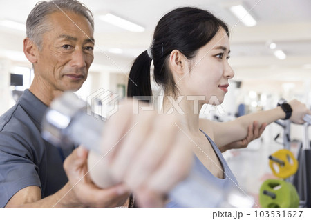 フィットネスジムでパーソナルトレーナーをつけてトレーニングをする若い女性 フィットネスジムでパーソナルトレーナーをつけてトレーニングをする若い女性 103531627