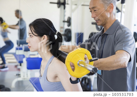 フィットネスジムでパーソナルトレーナーをつけてトレーニングをする若い女性 フィットネスジムでパーソナルトレーナーをつけてトレーニングをする若い女性 103531703