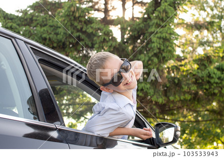 A cute boy climbed out of the car window wearing sunglasses and laughing 103533943