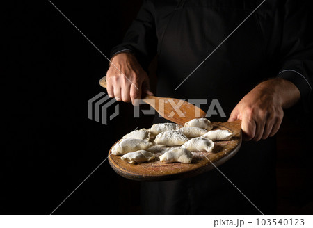 The chef prepares meat dumplings for lunch. Concept for a hotel menu on a black background with space for advertising The chef prepares meat dumplings for lunch. Concept for a hotel menu on a black background with space for advertising 103540123