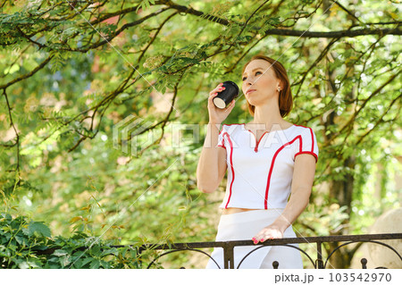 Red-haired woman in white sport shirt with a coffee cup in hand outdoors 103542970