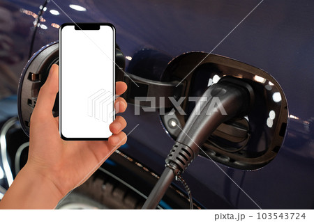 Hand with smartphone on a background of electric car . White screen, you can add your content here.. 103543724
