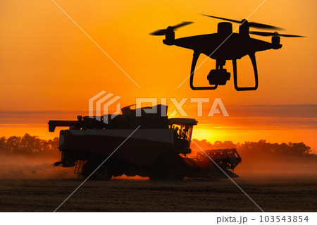 Silhouettes of combine harvester and drone 103543854