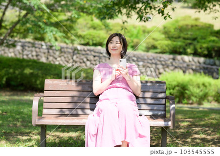 木陰でスマホを操作する若い女性 103545555