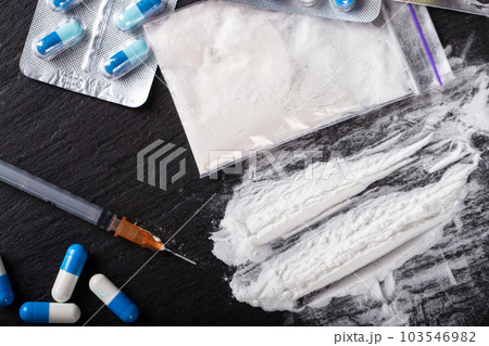 Drugs are scattered on the black table, there is a syringe and pills Drugs are scattered on the black table, there is a syringe and pills 103546982