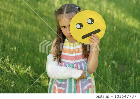 Sad girl with arm injury holds upset emoticon face.  Different faces of emojis displaying human emotions 103547737