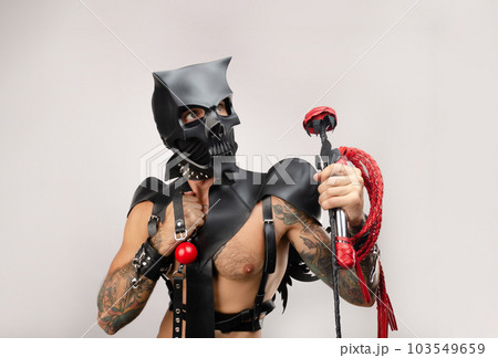 A sexy man in bdsm wearing a demon mask with a whip wearing a leather cloak with leather handcuffs and partuppets on a white background A sexy man in bdsm wearing a demon mask with a whip wearing a leather cloak with leather handcuffs and partuppets on a white background 103549659