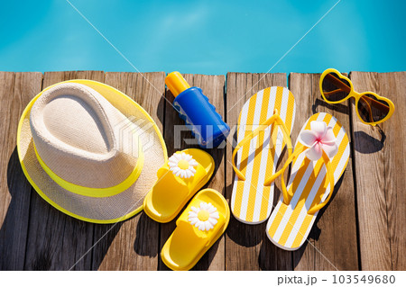 Beach hat, flip-flops and sunglasses on wooden planks near swimming pool Beach hat, flip-flops and sunglasses on wooden planks near swimming pool 103549680