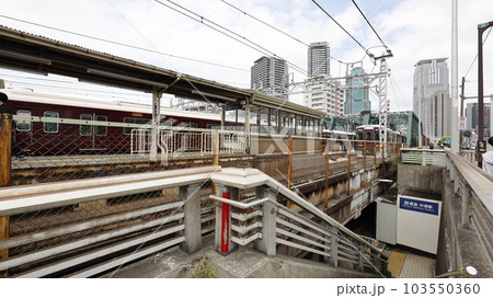阪急電車の中津駅、階段を下りたところにある出入口と駅ホーム（左側）に入る電車 103550360