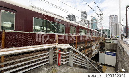 阪急電車の中津駅、階段を下りたところにある出入口と駅ホーム（左側）に入る電車 103550361