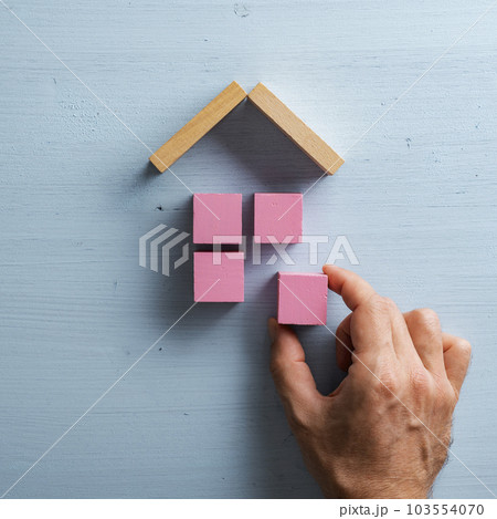 Male hand making a house or home of pink wooden blocks with a roof 103554070