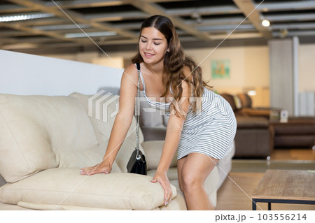 Young woman carefully examines sofa before buying and checks elasticity of surface with hand 103556214