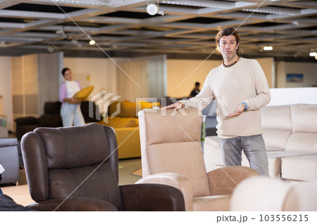Male furniture salesperson presenting armchairs for sale in furniture showroom 103556215