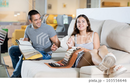 In exhibition hall,couple sat down on gray sofa and keep sets of upholstery material samples In exhibition hall,couple sat down on gray sofa and keep sets of upholstery material samples 103556646