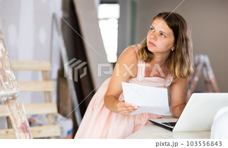 Woman construction manager checking project documentation, using laptop 103556843