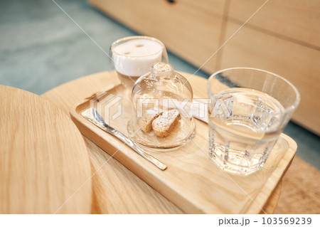 Cup of coffee cappuccino with cantuccini and a glass of water on a wooden tray. Coffee with milk, a cookie and a glass with water on a glass table. 103569239