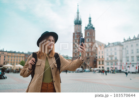 Young stylish woman tourist making selfie photo of the famous St. Mary's Basilica on the Market square during the sunrise in Krakow, Poland 103570644
