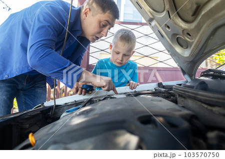 Dad shows his son where to fill in the coolant in the engine compartment. Topping up antifreeze in the car cooling system. Expansion tank near the engine. Red liquid 103570750