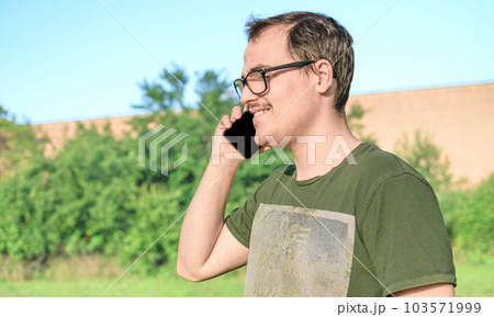 Young man with eyeglasses and green t-shirt talking on cell phone at the park 103571999