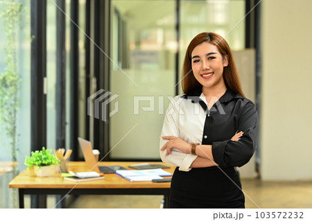 Confident millennial businesswoman wearing stylish clothes standing with crossed arms and smiling to camera Confident millennial businesswoman wearing stylish clothes standing with crossed arms and smiling to camera 103572232