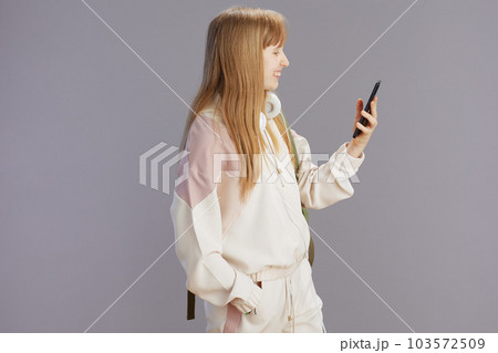 smiling trendy teen girl in beige tracksuit using phone 103572509