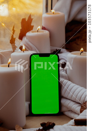 Green screen chromakey mobile phone app copy space on background of aesthetic atmosphere Autumn leaves spices and candle on knitted white sweater in warm yellow lights. Still life. Raining 103573178