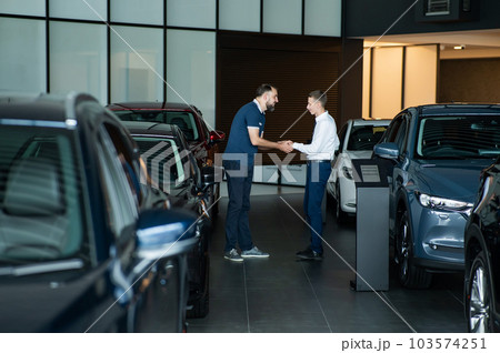 Seller and buyer shake hands in a car dealership. Caucasian man buys a car. 103574251