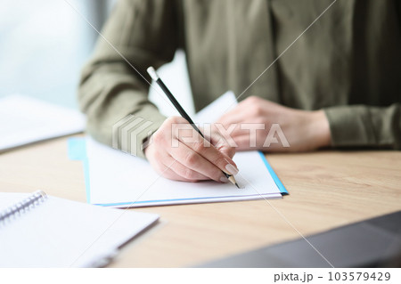 Woman writes on paper sheet with pencil sitting at desk 103579429