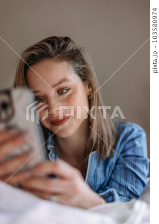 Young woman lying on a bed and scrolling her smartphone. Young woman lying on a bed and scrolling her smartphone. 103580974