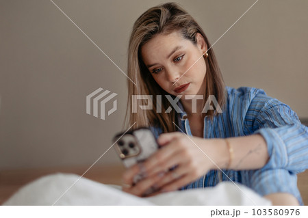 Young woman lying on a bed and scrolling her smartphone. Young woman lying on a bed and scrolling her smartphone. 103580976