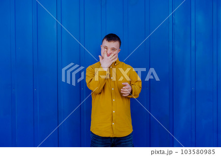 Happy young man with Down syndrome smiling and looking at camera against blue background. Happy young man with Down syndrome smiling and looking at camera against blue background. 103580985