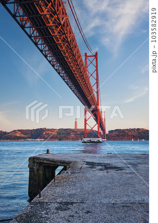 View from under of 25 de Abril Bridge famous tourist landmark over Tagus river, Christ the King monument and quay. Lisbon, Portugal View from under of 25 de Abril Bridge famous tourist landmark over Tagus river, Christ the King monument and quay. Lisbon, Portugal 103582919