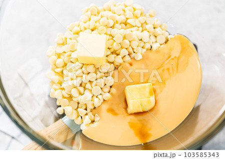 Melting white chocolate chips and other ingredients in a glass mixing bowl over boiling water to prepare candy cane fudge. Melting white chocolate chips and other ingredients in a glass mixing bowl over boiling water to prepare candy cane fudge. 103585343