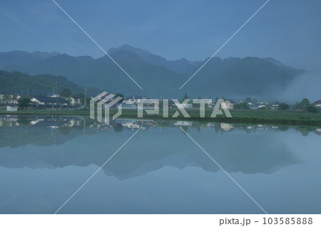北杜市白州町、晴れ行く霧。水田の水面に映る山並みと街並み 103585888