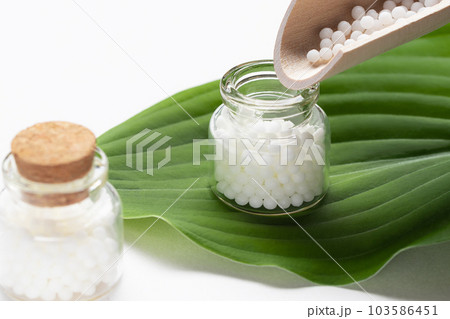 Pouring homeopathic granules from a wooden scoop into a bottle 103586451