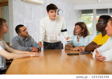 Young man instructor explaining the topic to group of guys around the table Young man instructor explaining the topic to group of guys around the table 103588390