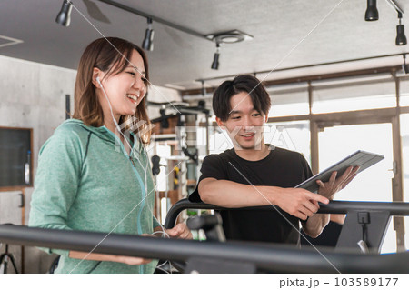 パーソナルトレーニングを受ける笑顔のアジア人女性と指導するインストラクターの男性 103589177