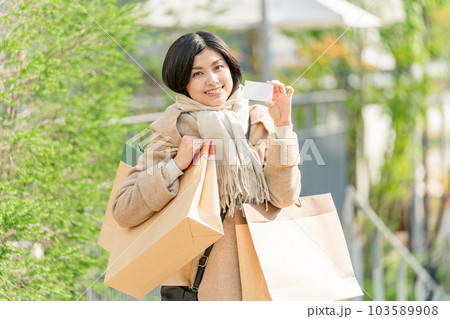 ベージュのコートを着て紙袋をたくさん持ってクレジットカードを持つ若い女性　お買い物イメージ 103589908