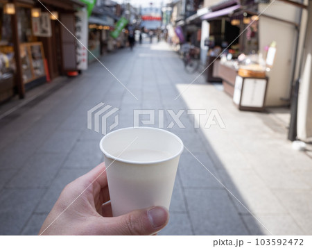 【日本】閑散とした柴又帝釈天前の石畳の通りで買った甘酒の入った紙コップを持つ手 103592472