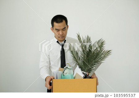 A male office worker is unhappy with being fired from a company packing things into cardboard boxes. The young man was stressed and disappointed by being fired. concept of layoffs and unemployment 103595537