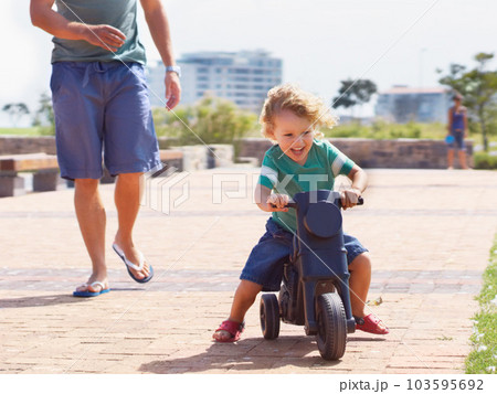 Happy, toy and motorbike with child and father playing in park for bonding, laugh and fun. Smile, happiness and energy with man and young boy riding on scooter for playful, youth and summer Happy, toy and motorbike with child and father playing in park for bonding, laugh and fun. Smile, happiness and energy with man and young boy riding on scooter for playful, youth and summer 103595692
