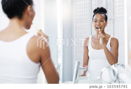 Woman brushing teeth in bathroom, mirror and oral hygiene, morning routine with toothbrush and dental health. Female person at home, grooming and self care, clean mouth with toothpaste and wellness 103595791
