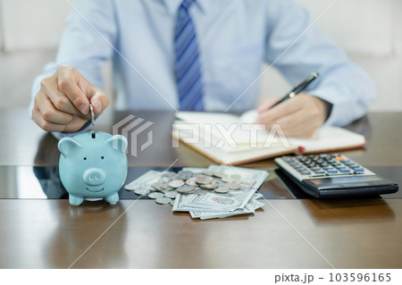 Man putting coin into piggy bank. Saving money with coins Step into a business that is growing to be successful and save for retirement concepts Man putting coin into piggy bank. Saving money with coins Step into a business that is growing to be successful and save for retirement concepts 103596165