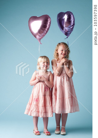 Were never giving these up. Shot of two little girls holding heart balloons against a studio background. 103597398