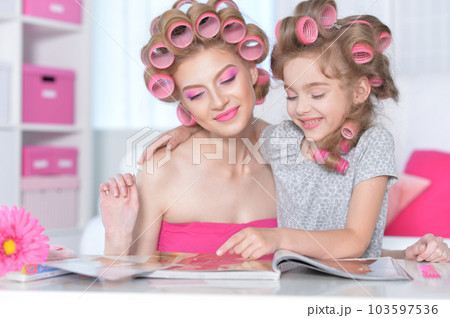 Mom and daughter with hair curlers reading magazine 103597536