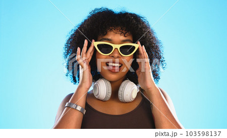 Trendy black woman face isolated on blue background for beauty, cosmetics and fashion of gen z lifestyle. Confident african american person or model with cool sunglasses and headphones for summer Trendy black woman face isolated on blue background for beauty, cosmetics and fashion of gen z lifestyle. Confident african american person or model with cool sunglasses and headphones for summer 103598137