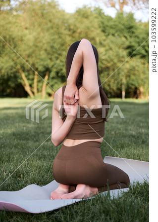 A young woman sits in a lotus position and meditates in the park on a warm summer day. 103599222